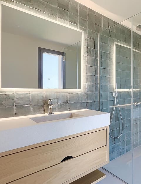 Modern bathroom featuring a light wood vanity, a glass-enclosed walk-in shower with textured blue tiles, and a white wall-mounted toilet.