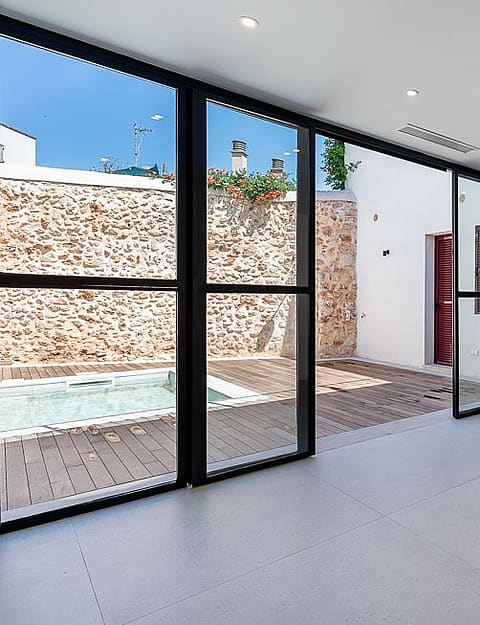 Modern open-plan living room with large floor-to-ceiling sliding glass doors opening onto a stone-walled terrace with a plunge pool.