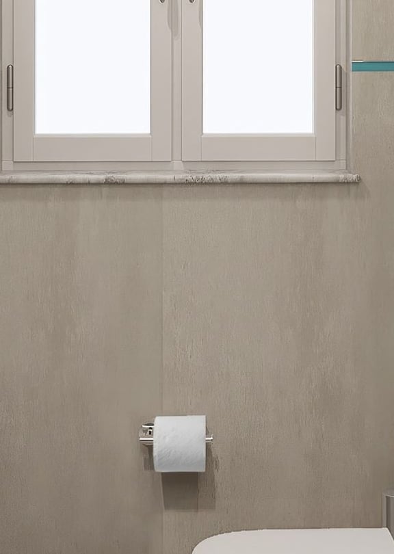 Interior view of a minimalist bathroom featuring grey stone tiles, a white wall-mounted toilet, and a small window.