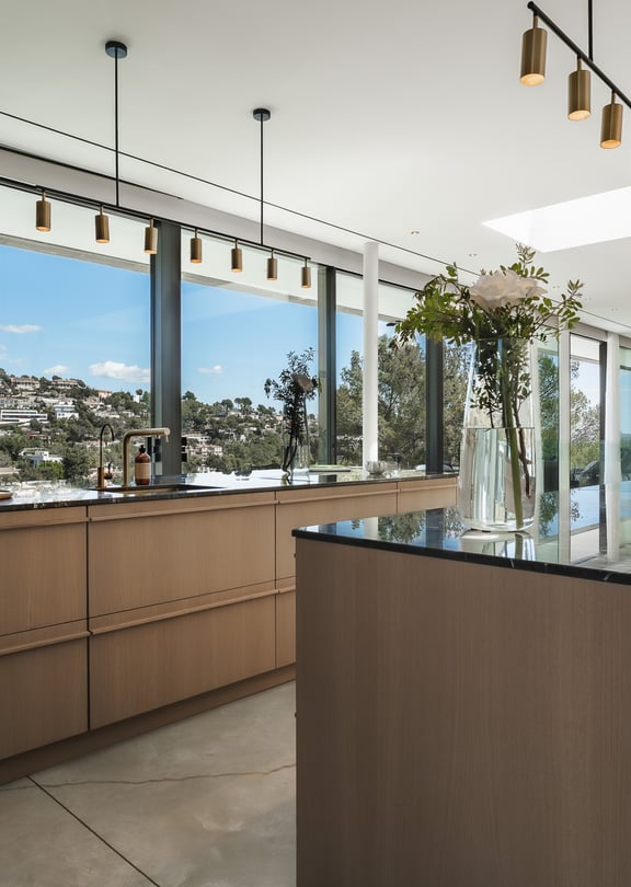 Contemporary kitchen featuring a wooden island with bar seating, dark countertops, and windows overlooking green hills.