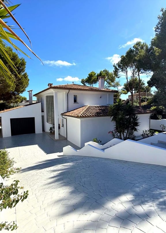 Front elevation of a white two-storey villa with terracotta roof, double garage and wide paved driveway