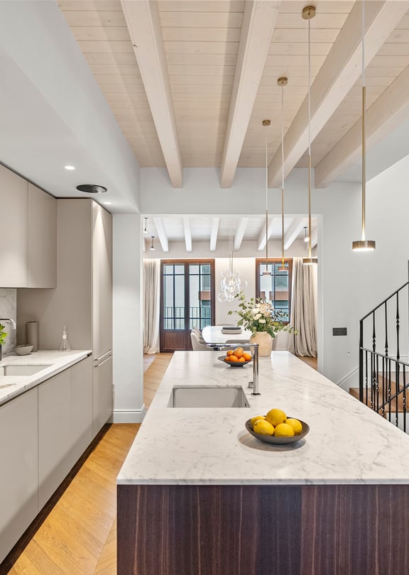 Kitchen island with marble top and dark wood base beside a staircase with black iron railings and exposed ceiling beams.