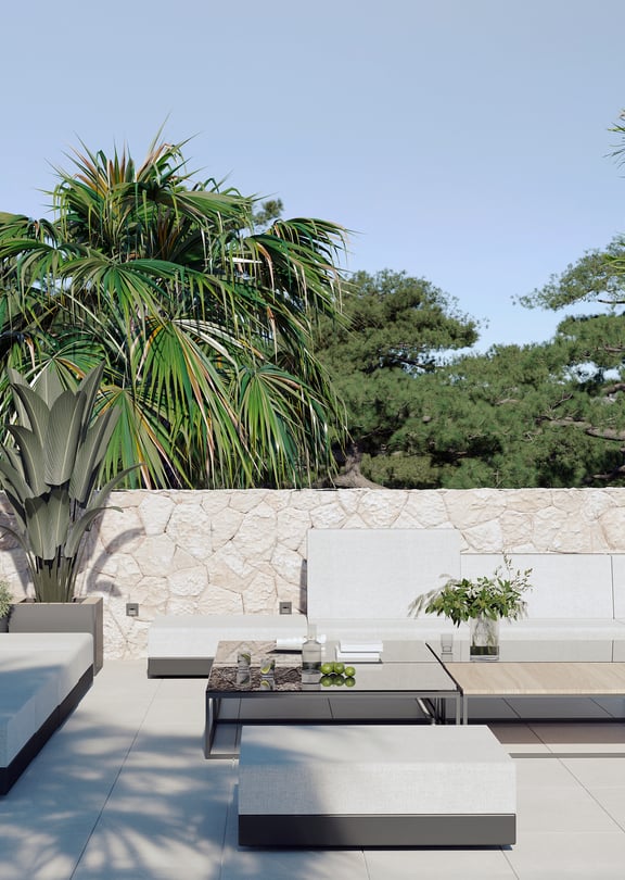 A contemporary outdoor terrace featuring low-profile modular white sofa seating and wooden coffee tables against a natural stone wall.