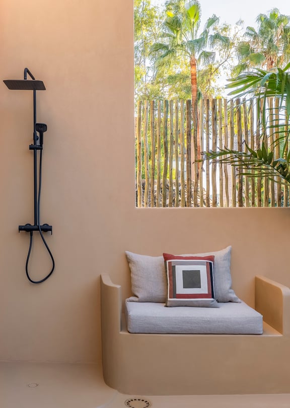 Modern outdoor shower with black fixtures next to a built-in masonry bench and tropical plants.