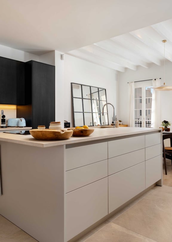 Open kitchen with black cabinetry, a pale stone-topped island, and a dining table and French doors visible beyond.