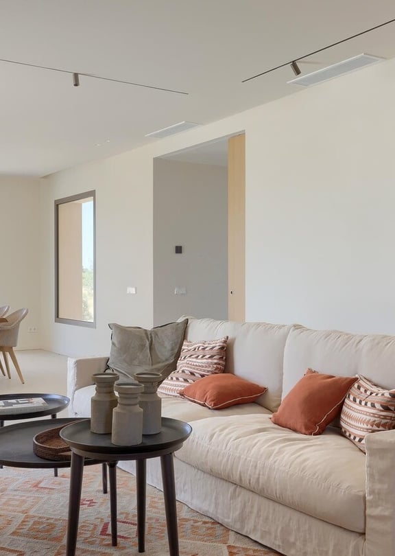 An open-concept living and dining space with a cream fabric sofa, nested coffee tables, and a wooden dining set near a large window.