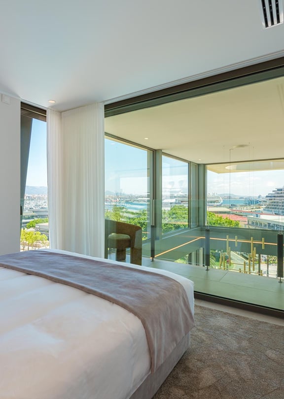Dormitorio moderno con cama grande, decoración neutra y ventanales correderos con salida a la terraza.