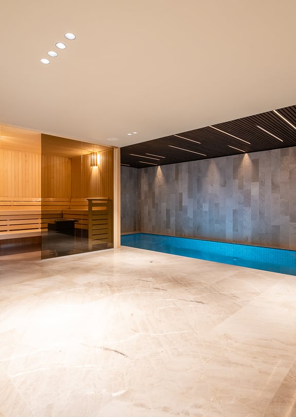 Indoor spa area featuring a tiled lap pool, sauna with glass door, polished stone flooring, and recessed ceiling lighting.