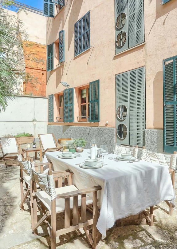 Outdoor terrace in a historic Old Town building with a dining table, folding wooden chairs, and green shutters.