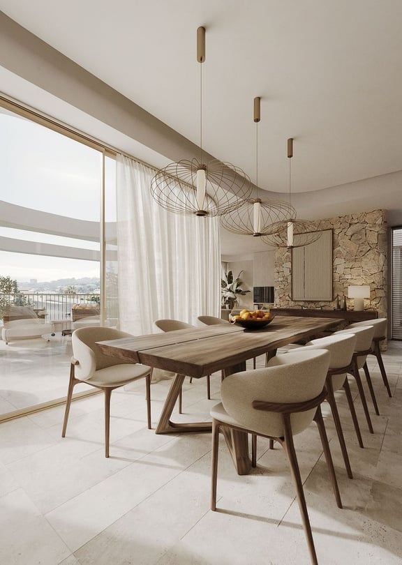Dining area with long wooden table, cream upholstered chairs, and a natural stone feature wall, opening onto a balcony.