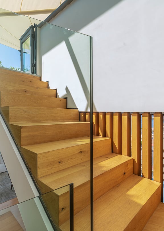 A modern interior staircase featuring solid oak treads and vertical timber slat railings, complemented by a transparent glass balustrade.