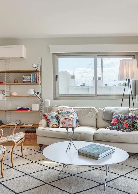 Bright living room featuring a neutral sofa, patterned armchairs, metal shelving, and a large window leading to a terrace.