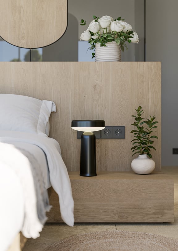 Close-up of a modern bedside setup with a textured oak headboard, black designer lamp, and a small ceramic vase.