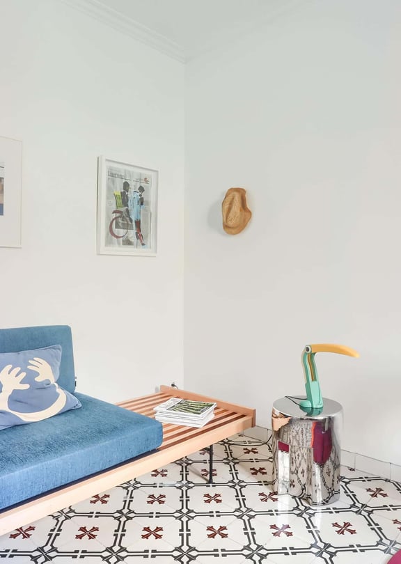 A small living space featuring a blue upholstered daybed, patterned floor tiles, a chrome side table, and a modern chair.