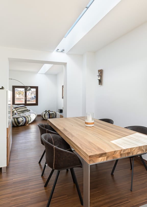 Modern dining area with oak table, dark chairs, and a long linear skylight over dark wood floors.