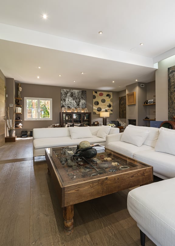 Spacious living room featuring white modular sofas, a stone-topped coffee table, and beige tiled floors under recessed lighting.