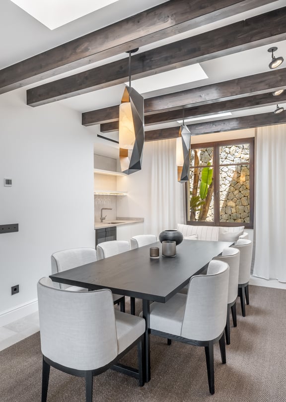 Modern dining room featuring a dark wood table, grey upholstered chairs, exposed ceiling beams, and integrated skylights.