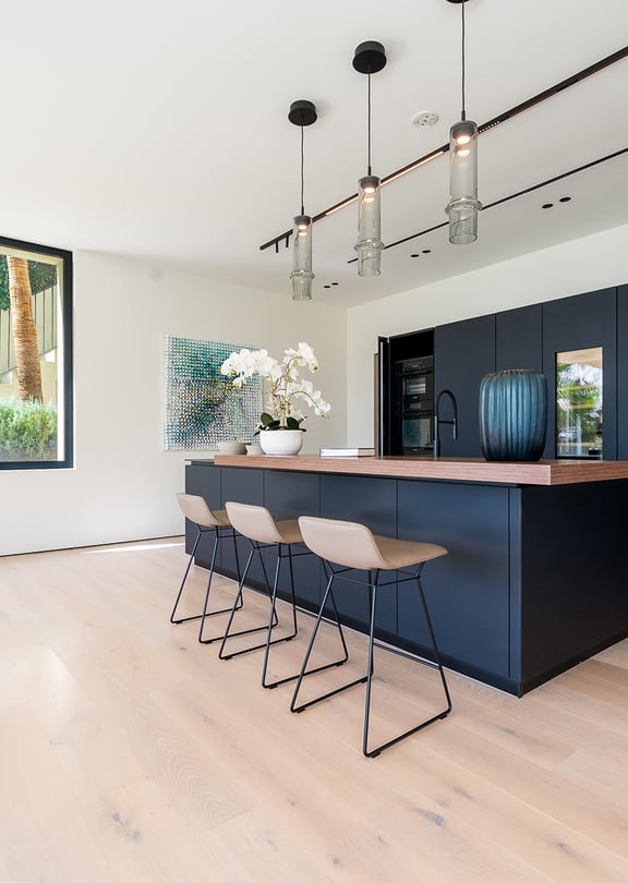 Modern open-plan kitchen featuring a dark matte island, light oak hardwood floors, and three pendant lights in Son Vida.