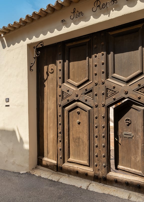 Heavy dark wood gate with iron studs and an inset pedestrian door set into a stone wall under tiled eaves.
