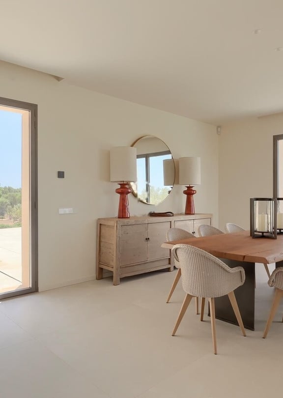 Dining room featuring a wooden table, upholstered chairs, a sideboard with lamps, and large glass doors opening to a garden.
