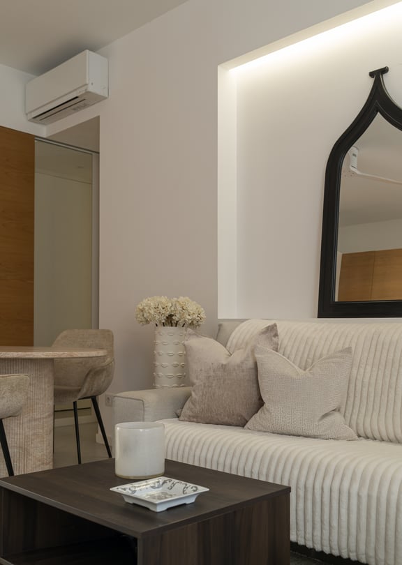 A modern living area featuring a ribbed beige sofa, dark wood coffee table, and an arched black-framed wall mirror.
