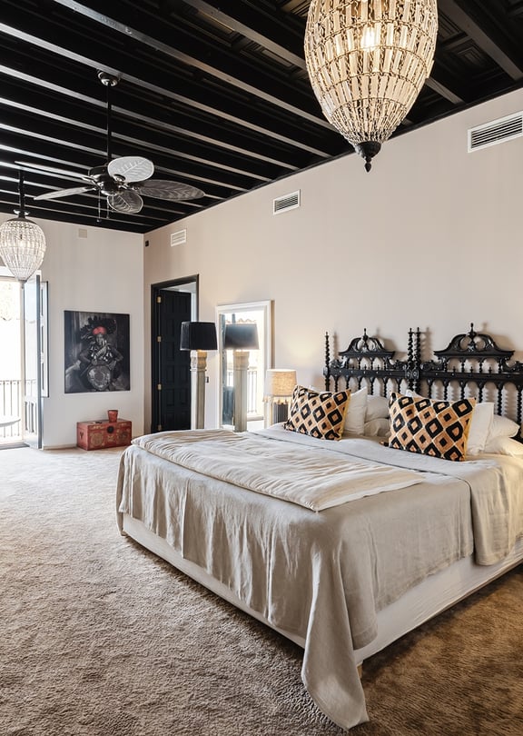 A spacious master bedroom in a Sencelles townhouse featuring a black exposed beam ceiling, a wrought iron bed, and neutral walls.