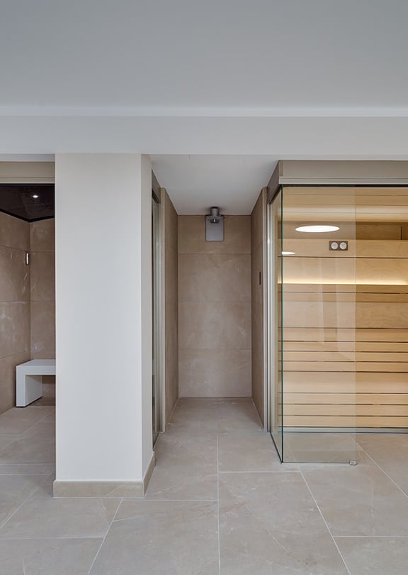 Glass-enclosed steam room with marble-effect tiles alongside a Finnish sauna with cedar benching and warm interior lighting