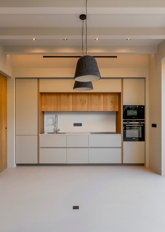 Modern kitchen with white and oak cabinetry, micro-cement floors, and sliding glass doors leading to a sun-drenched terrace.