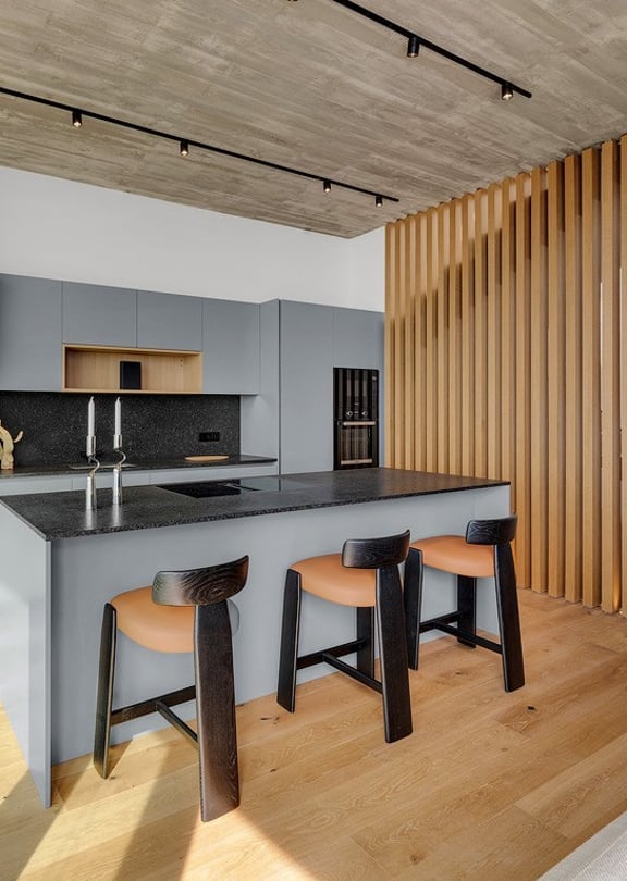 Modern open-plan kitchen featuring a gray island, oak wood slat room divider, light wood flooring, and track lighting.