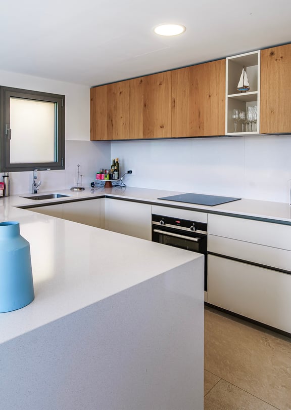 Modern U-shaped kitchen with white stone countertops, wood-veneer upper cabinets, and integrated appliances.