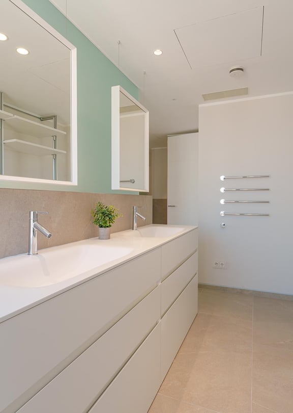 Baño moderno con doble lavabo blanco, pared verde salvia, dos espejos rectangulares y estanterías integradas.