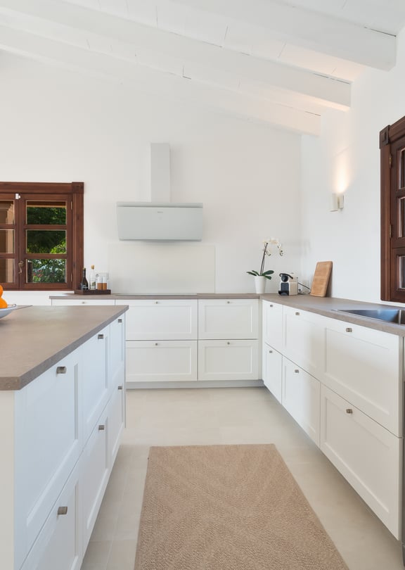 Cocina con muebles blancos, encimeras de piedra y marcos de madera bajo techos abovedados de madera blanca.