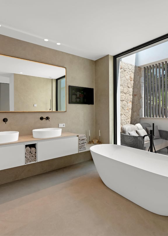 Spa-style bathroom with freestanding white bath, double vessel sinks, stone wall cladding and glazed opening to private terrace