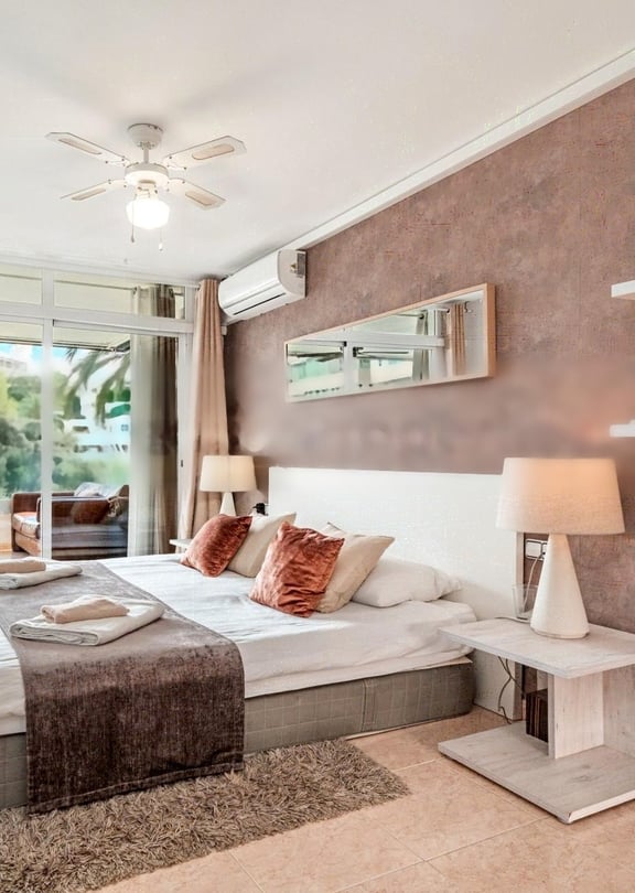A modern bedroom featuring a large bed with neutral linens, a textured terracotta feature wall, and glass sliding doors leading to a private terrace.