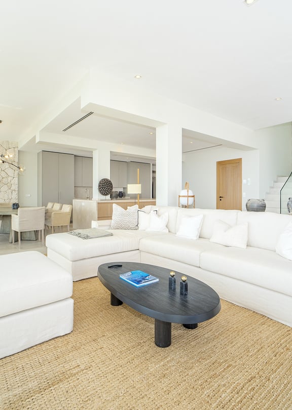 Bright open-plan living room in Illetas with white sectional sofa, oval coffee table, and a large textured jute rug.