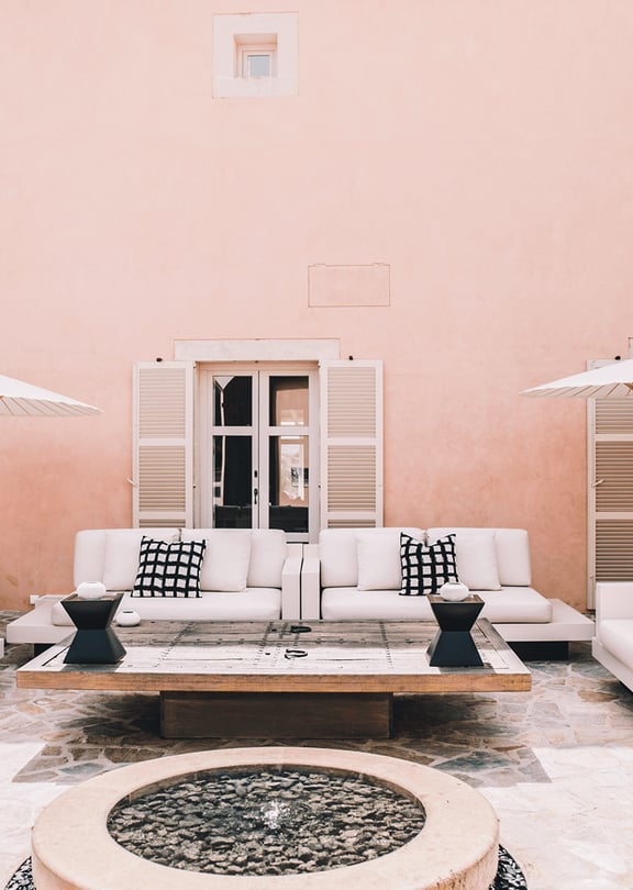 Outdoor courtyard of a Finca with pink plaster walls, white sofas, and stone flooring.