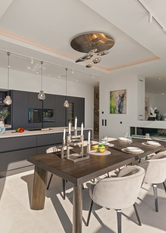 Modern open-concept interior featuring a dark grey kitchen island, a wooden dining table with light chairs, and recessed ceiling lighting.