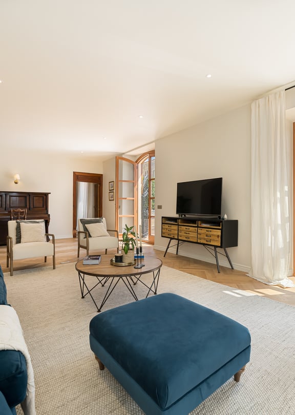 Living area featuring blue velvet tufted sofas, light herringbone wood floors, a dark piano, and arched patio doors.