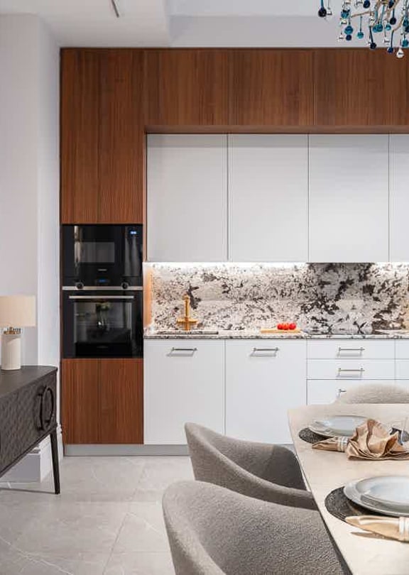 Modern kitchen with white cabinets, dark wood trim, and a patterned marble backsplash. Includes a side console and dining table.