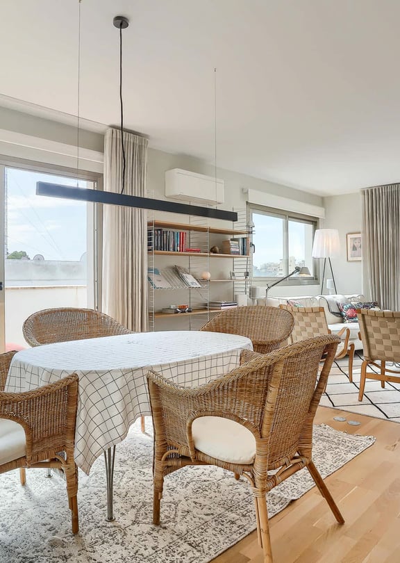 A bright dining area with a round table, wicker chairs, and large glass sliding doors opening onto a terrace with sea views.