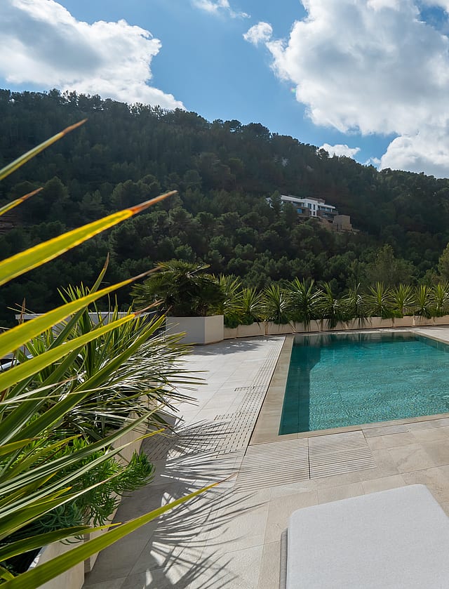 A rectangular swimming pool on a tiled terrace with white sun loungers, set against a multi-story villa with arched balconies.