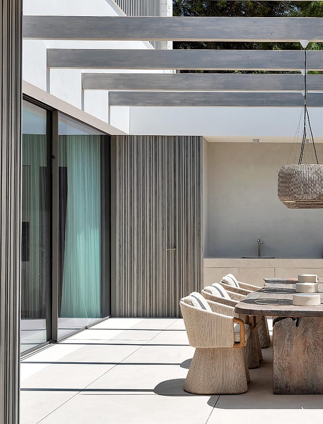 Covered outdoor dining area with exposed beam pergola, Mallorcan stone wall and wicker pendant lights