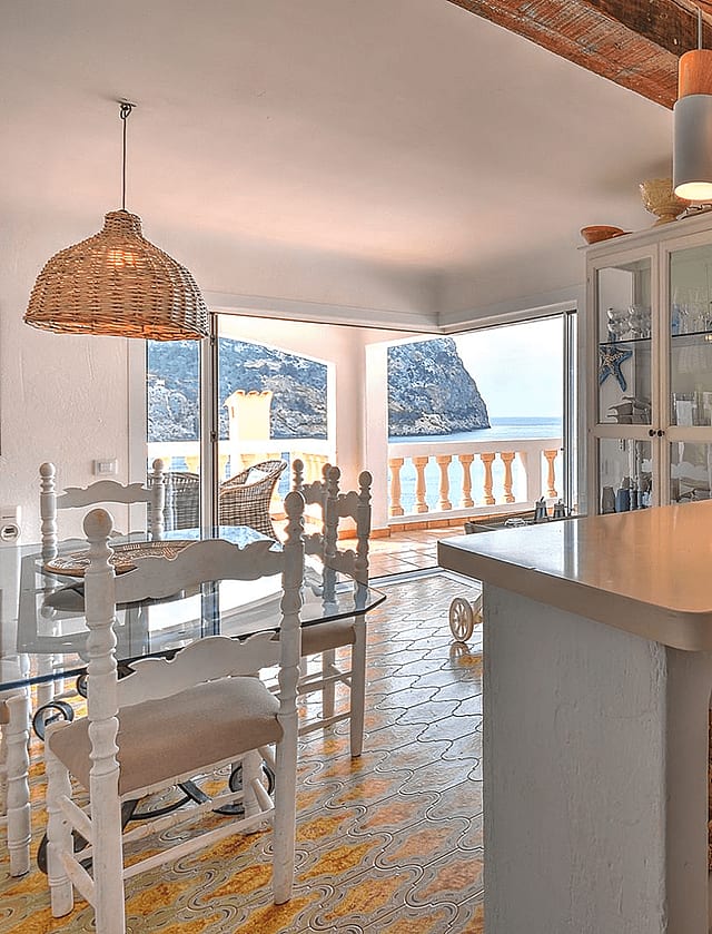 Kitchen and dining area with white cabinets, patterned tiled floor, and views of the Mediterranean coastline.