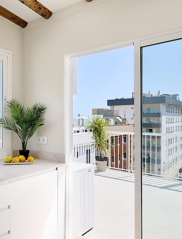 Modern kitchen corner with white cabinets and stone countertop, featuring large sliding glass doors opening to a balcony.