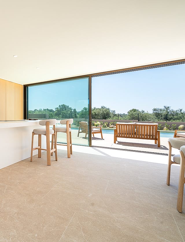 Modern open-plan kitchen with white island, light wood cabinetry, and floor-to-ceiling sliding glass doors opening to a terrace.