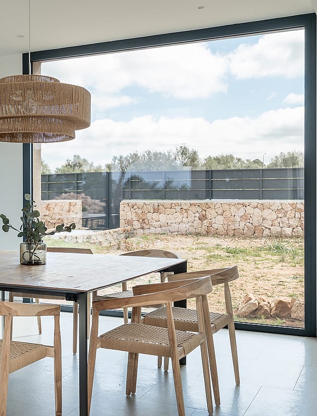 Dining area featuring a wooden table, woven chairs, and a large pendant light set against a window with mountain scenery.