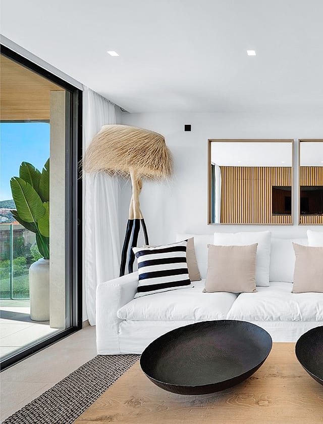 Modern living room featuring a white sofa with striped cushions, two black decorative bowls on a wooden coffee table, and vertical wood slat partitions.
