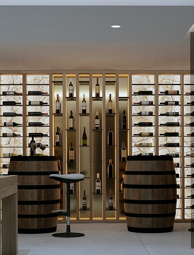 A modern wine cellar featuring backlit stone display walls, two wooden wine barrels used as tables, and bar stools.