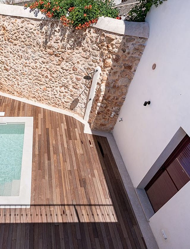 High-angle view of a small rectangular plunge pool surrounded by a wooden deck and high white walls with a natural stone feature wall.