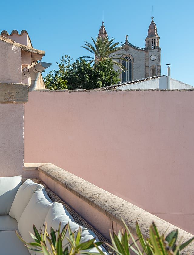 Outdoor terrace featuring exterior sofas, soft pink walls, and views towards the church tower in Calvià.